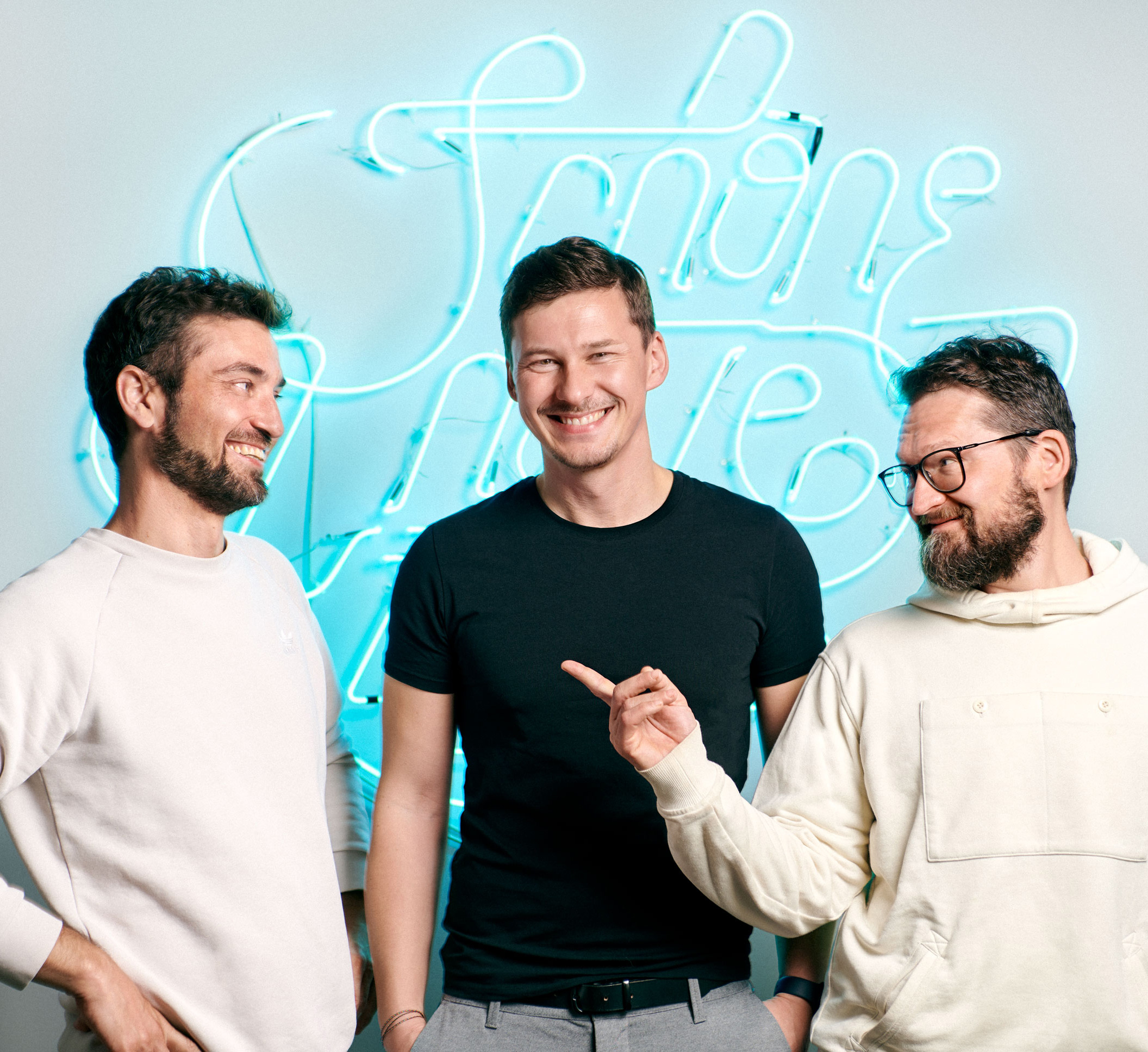 Ein Bild von Drei Männern, die nebeneinander vor einer SNK Neon-Leuchtschrift im SNK-Büro  stehen