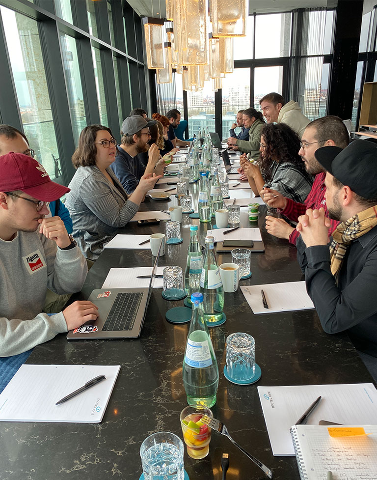 Foto: Viele Menschen sitzen mit Block und Stift an einer langen Tafel.